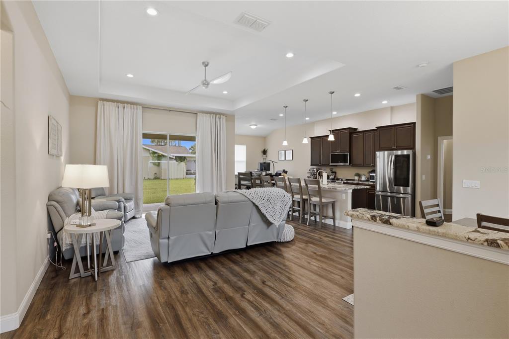 An open-concept living room and kitchen featuring wood-look flooring, dark cabinetry, and a sliding door — 50 PEPPER LANE, PALM COAST, FL