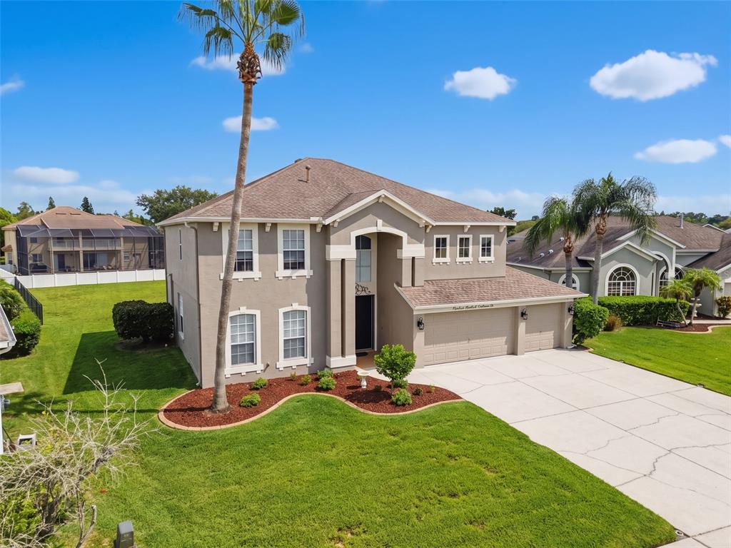 A two-story suburban house with a tan stucco exterior, a three-car garage, and a palm tree — 1900 CARDAMON DRIVE, TRINITY, FL