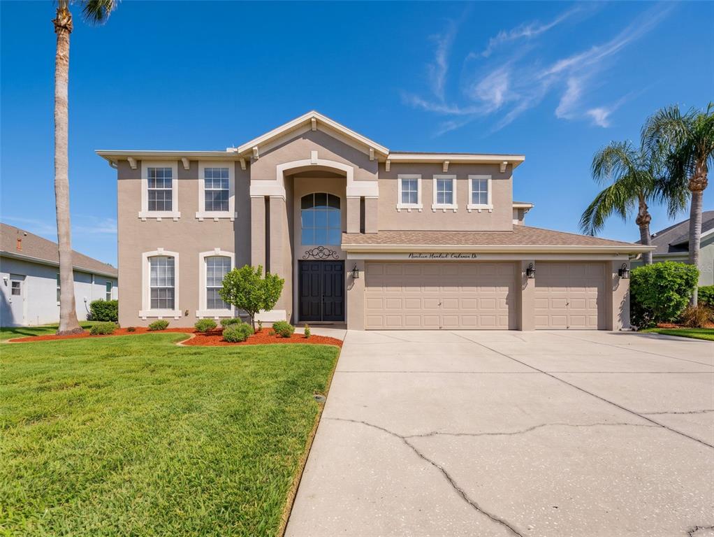 A two-story suburban house with a beige stucco exterior, a three-car garage, and a lawn — 1900 CARDAMON DRIVE, TRINITY, FL