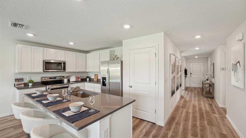 A modern kitchen features white cabinets, stainless steel appliances, a quartz island, and wood-look flooring — 11022 NW 167TH TERRACE, ALACHUA, FL