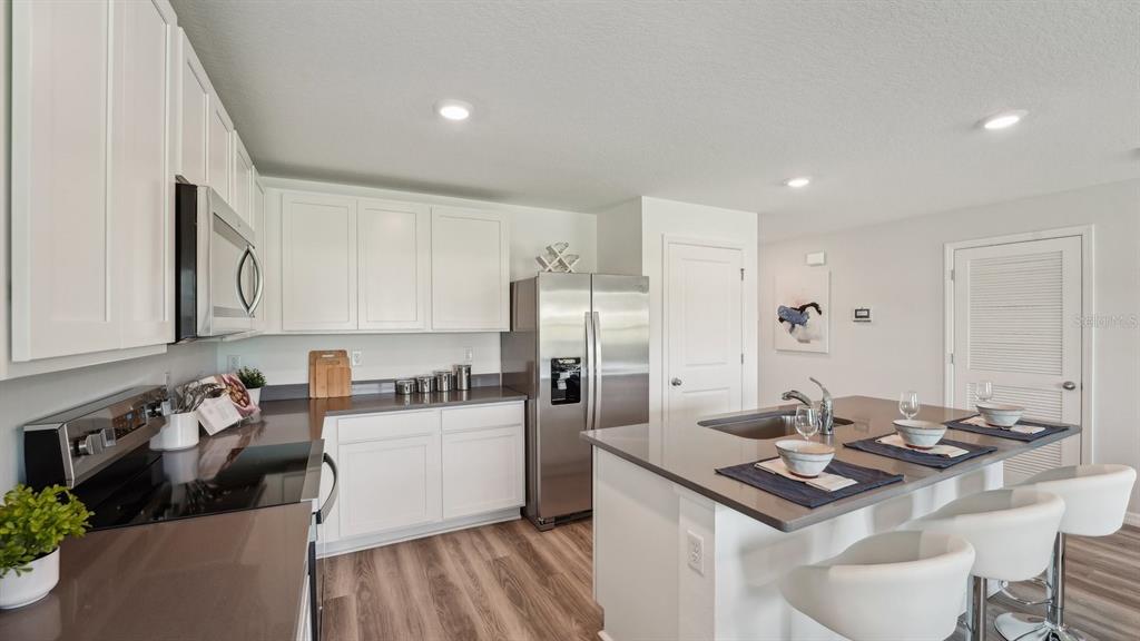 A modern kitchen features white cabinets, stainless steel appliances, and a central island with seating — 11022 NW 167TH TERRACE, ALACHUA, FL