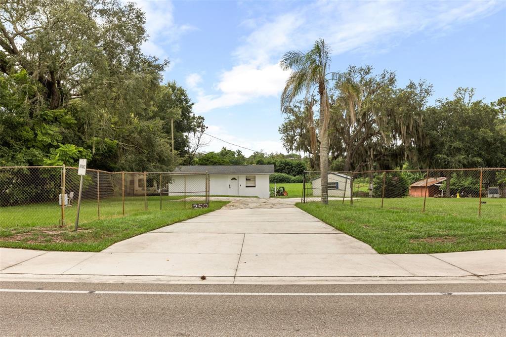 A concrete driveway leads to a small white house behind a chain-link fence — 250 LONGWOOD HILLS ROAD, LONGWOOD, FL