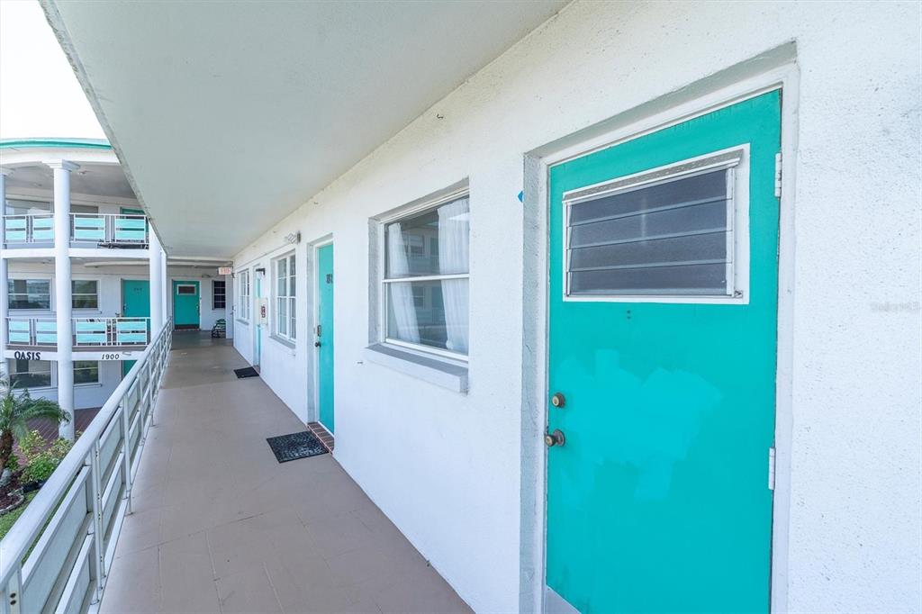 An exterior walkway features white walls, teal doors, and a metal railing overlooking a courtyard — 1900 59TH AVENUE N UNIT 212, ST PETERSBURG, FL