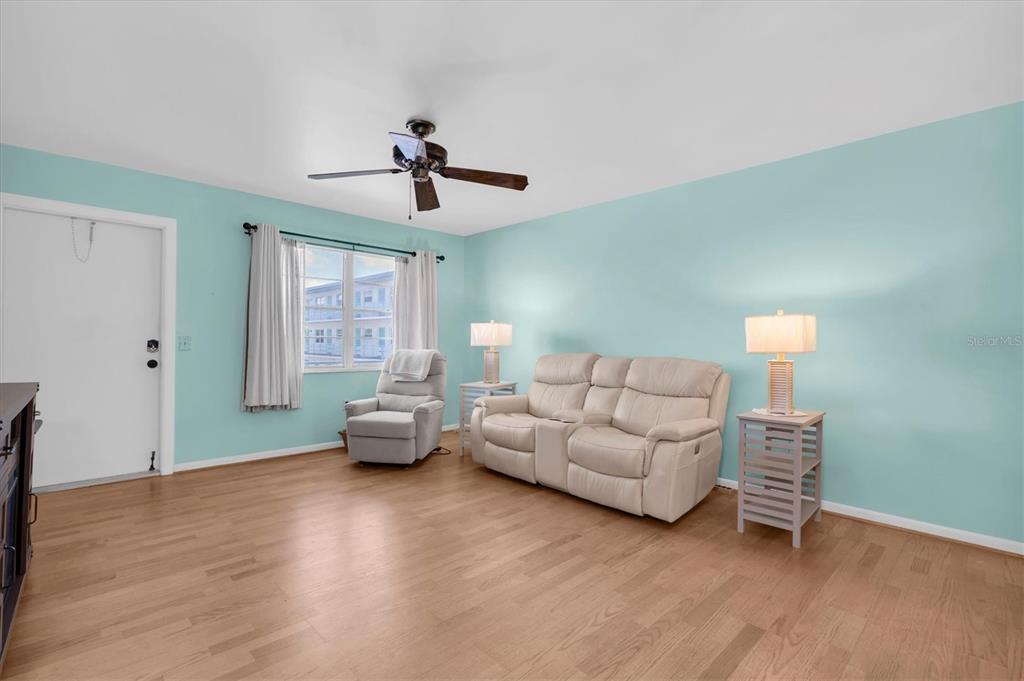 A living room with light blue walls, wood flooring, a ceiling fan, and beige furniture — 1900 59TH AVENUE N UNIT 212, ST PETERSBURG, FL