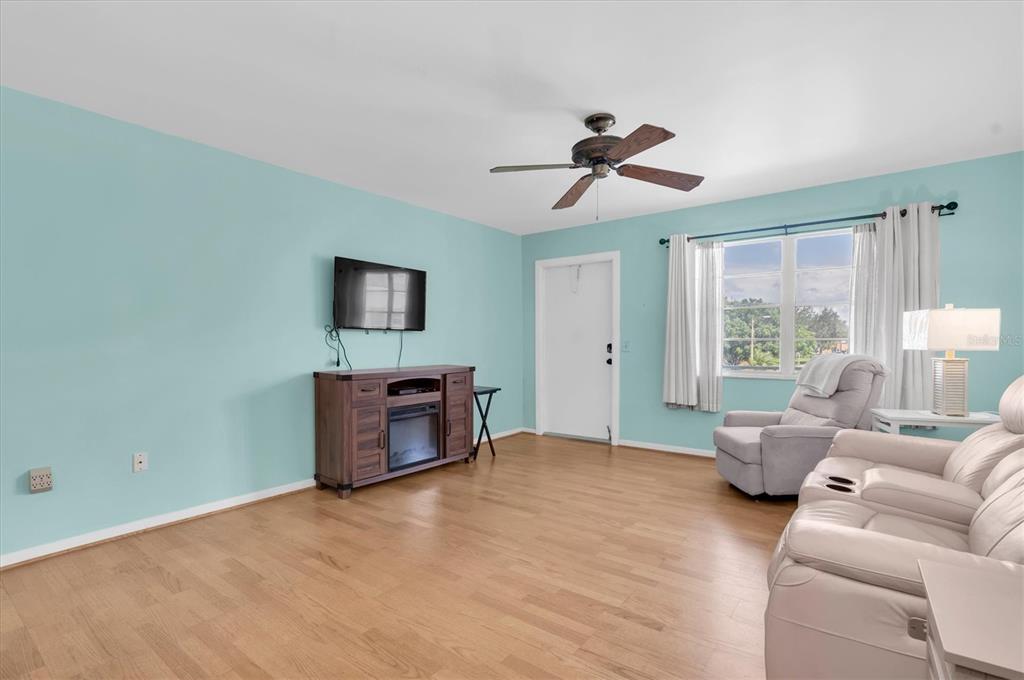 A living room with light blue walls, wood flooring, a ceiling fan, and furniture — 1900 59TH AVENUE N UNIT 212, ST PETERSBURG, FL