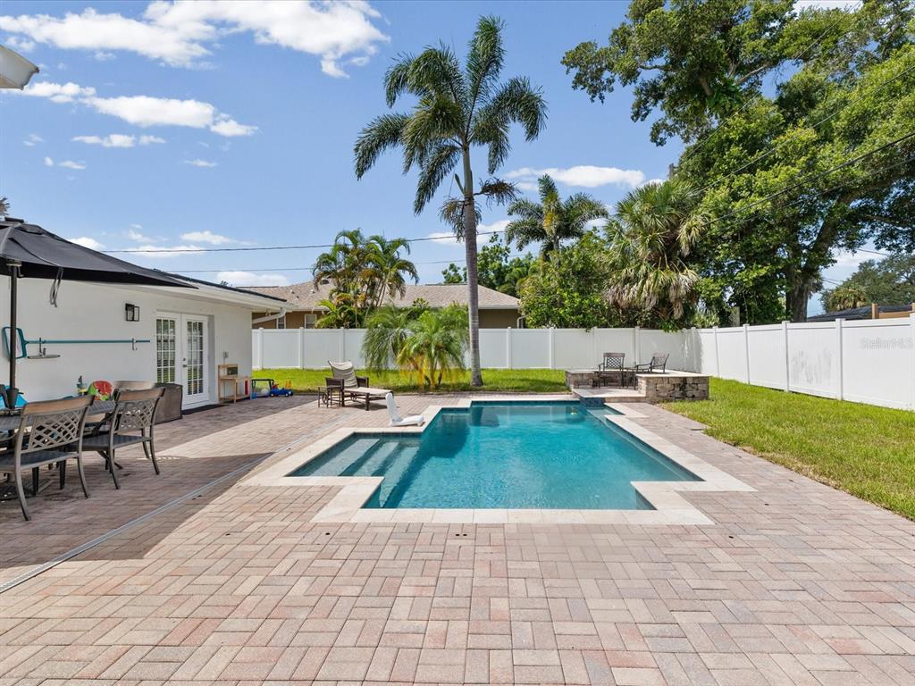 A backyard features a rectangular swimming pool, brick paver patio, palm trees, and white fencing — 118 LIVE OAK LANE, LARGO, FL