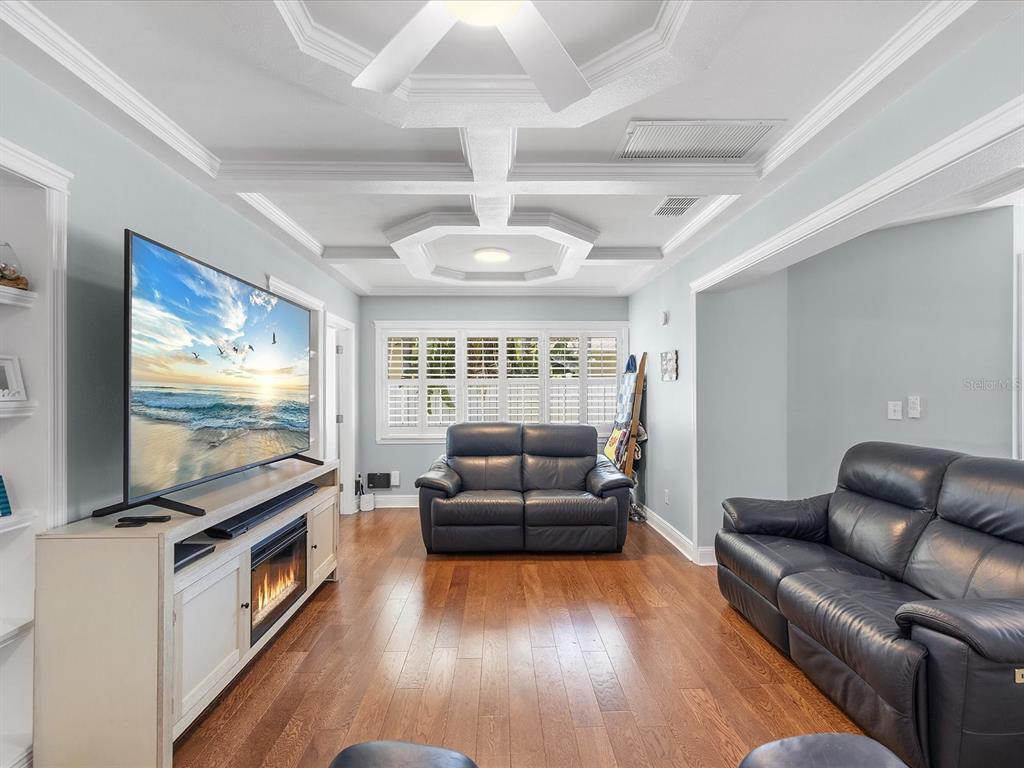 A living room features a coffered ceiling, hardwood floors, two dark leather sofas, and a television — 118 LIVE OAK LANE, LARGO, FL