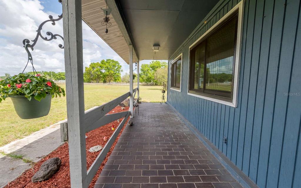 A covered brick porch with a wooden railing overlooks a grassy field — 3582 210TH PATH, LAKE CITY, FL