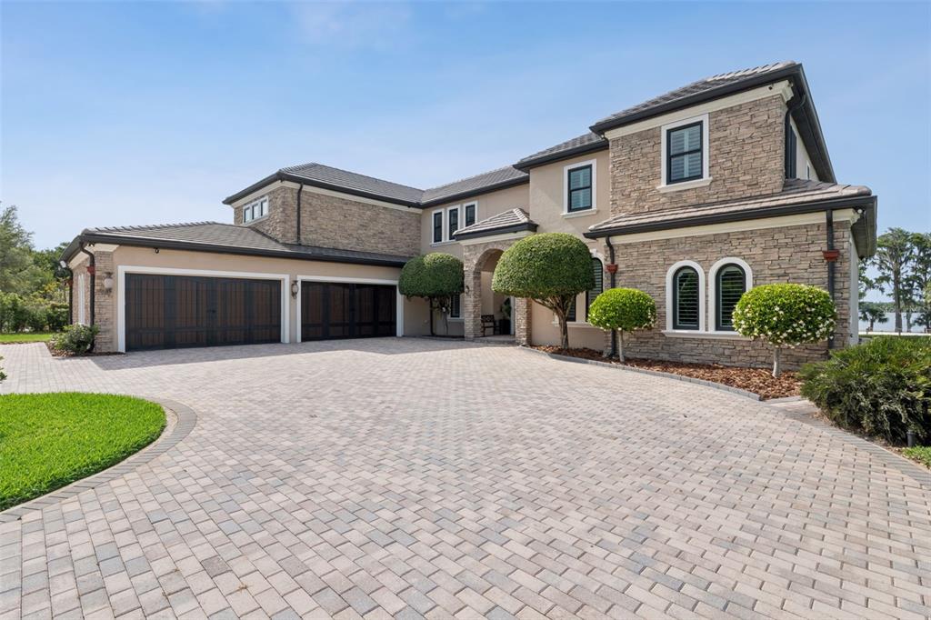 A large two-story house with a stone facade, dark garage doors, and a paved driveway — 746 LAKE MILLS ROAD, OVIEDO, FL