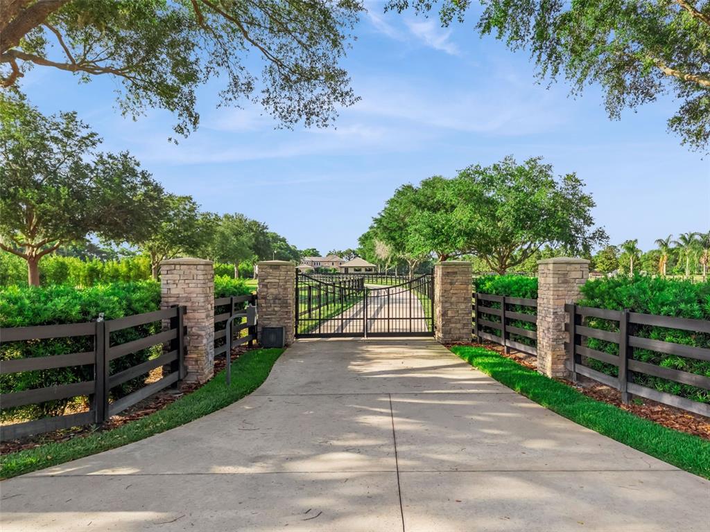A concrete driveway leads to a gated entrance flanked by stone pillars and wooden fencing — 746 LAKE MILLS ROAD, OVIEDO, FL