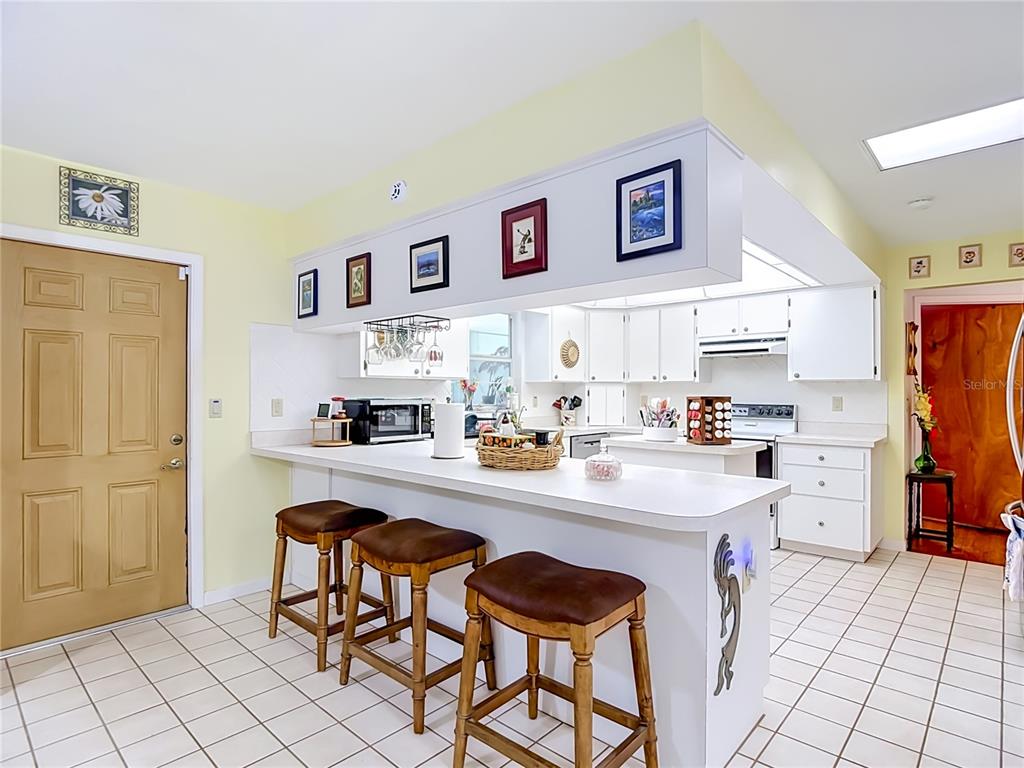 A kitchen features a white breakfast bar with three wooden stools and white cabinetry — 40312 SUNBURST DRIVE, DADE CITY, FL