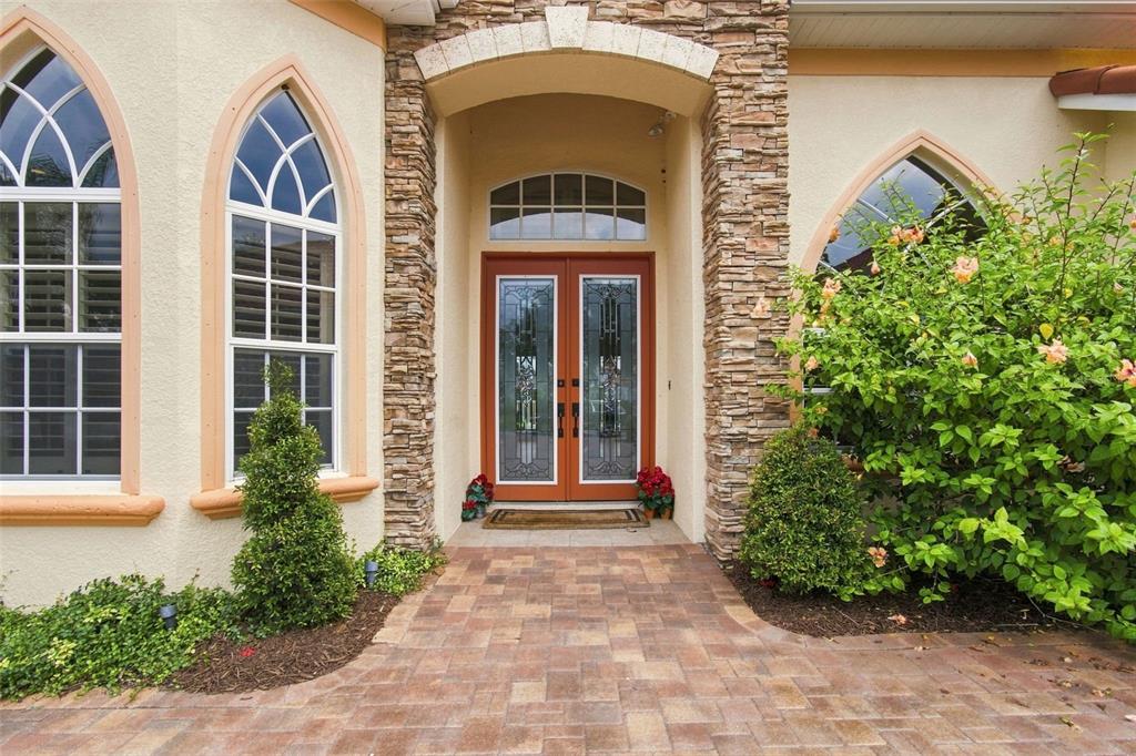 A stone-accented entryway features double glass doors, arched windows, and a paved walkway — 5102 DELACROIX DRIVE, BROOKSVILLE, FL