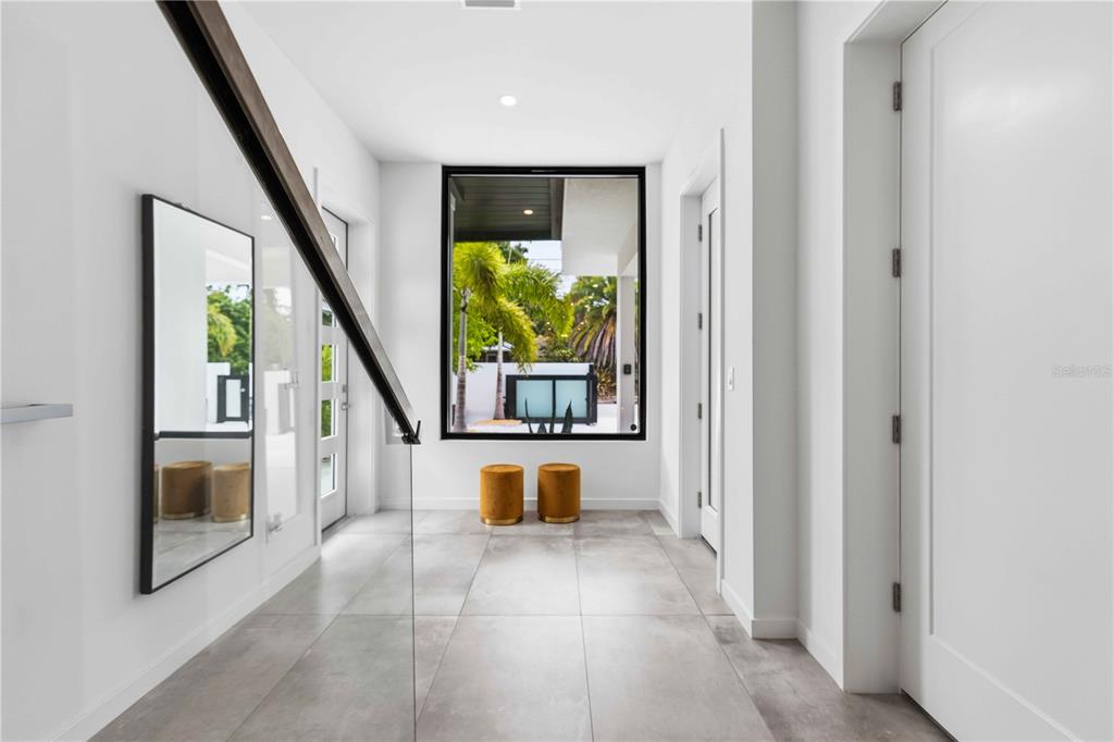 A modern hallway features large gray floor tiles, white walls, a glass railing, and windows — 1671 ARLINGTON STREET, SARASOTA, FL