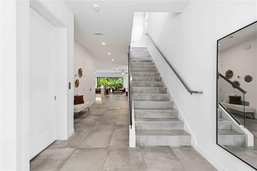 A modern entryway features large gray floor tiles, a staircase, and a large wall mirror — 1671 ARLINGTON STREET, SARASOTA, FL