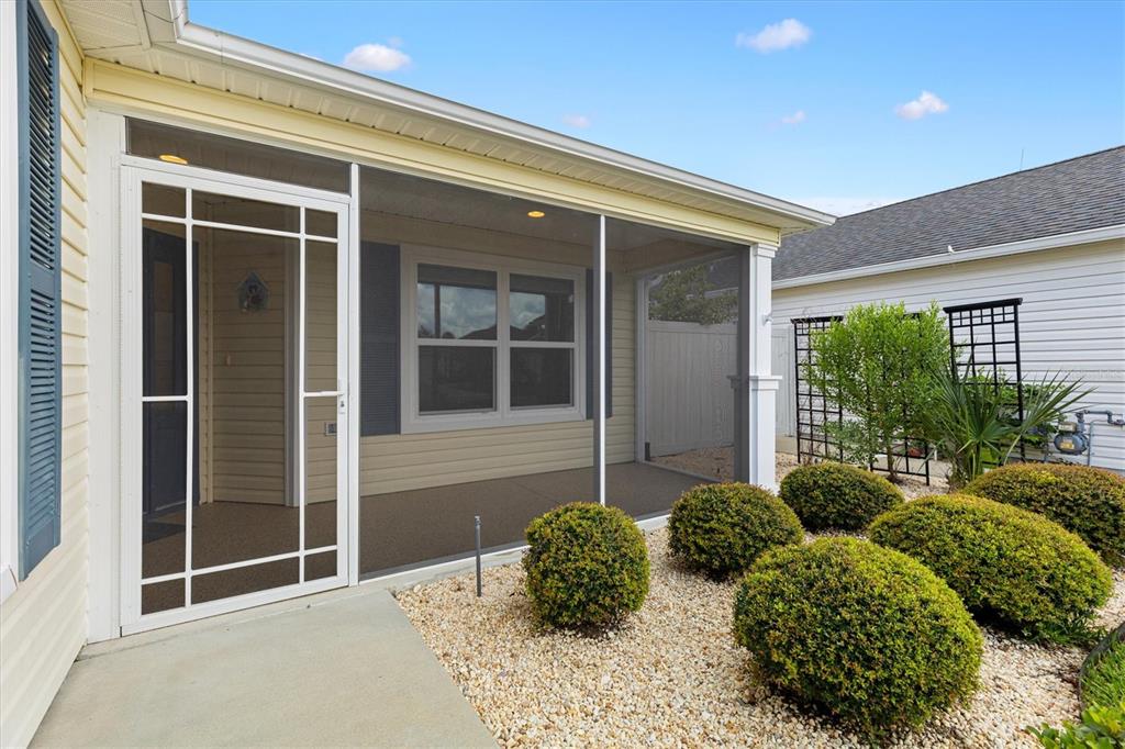 A screened-in porch with a white door sits beside a landscaped garden of round shrubs — 5805 CAMDYN COURT, THE VILLAGES, FL
