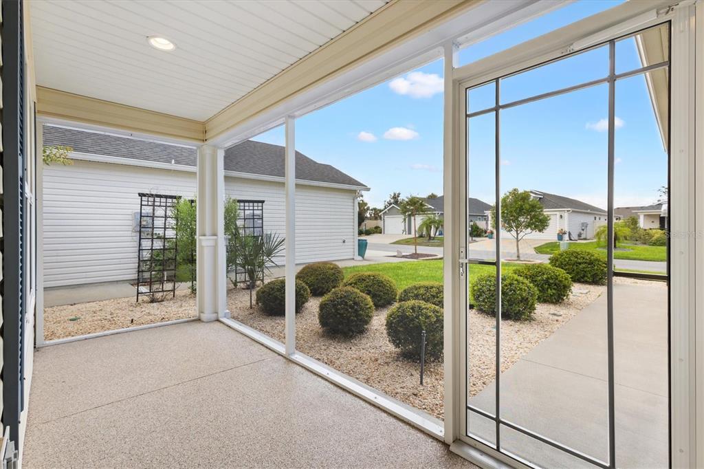 A screened-in porch with a concrete floor overlooks a landscaped yard and neighboring houses — 5805 CAMDYN COURT, THE VILLAGES, FL