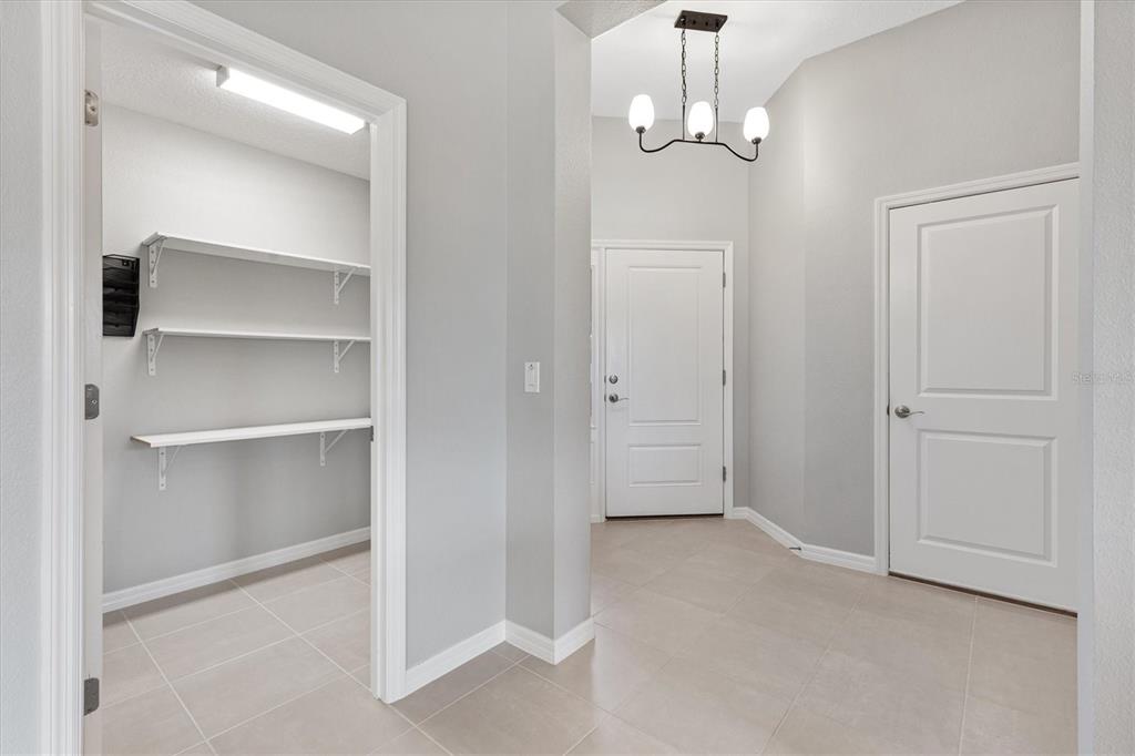 A tiled entryway features a white door, a chandelier, and an open storage closet — 5805 CAMDYN COURT, THE VILLAGES, FL