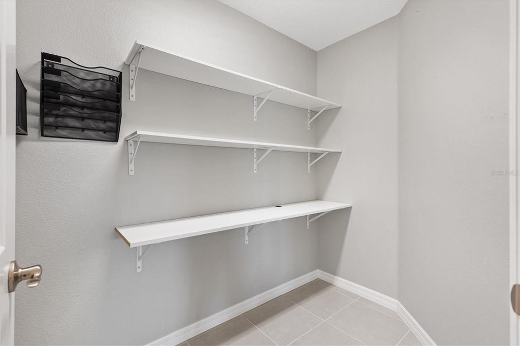 A small closet features three white shelves mounted on light gray walls above tiled flooring — 5805 CAMDYN COURT, THE VILLAGES, FL