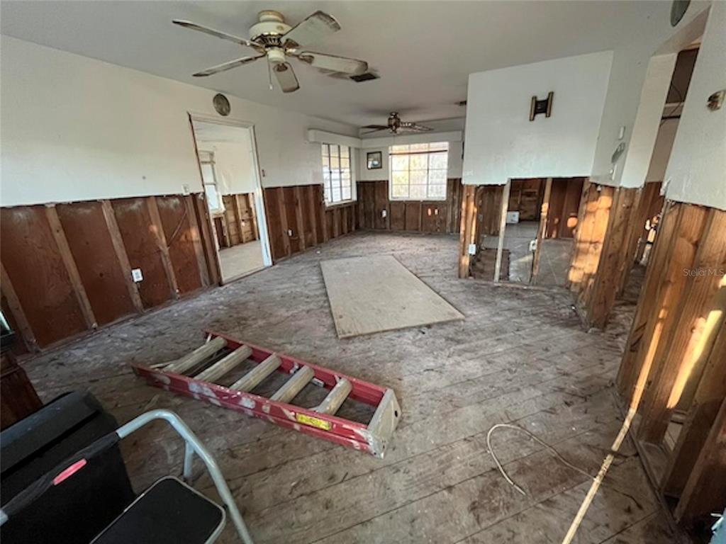 An interior room under renovation with exposed wall studs, wooden subflooring, and two ceiling fans — 7011 HIBISCUS AVENUE S, SOUTH PASADENA, FL