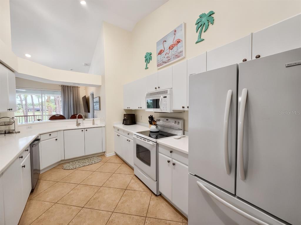 A kitchen features white cabinets, stainless steel appliances, tile flooring, and a vaulted ceiling — 8175 CELESTE DRIVE UNIT 1229, NAPLES, FL