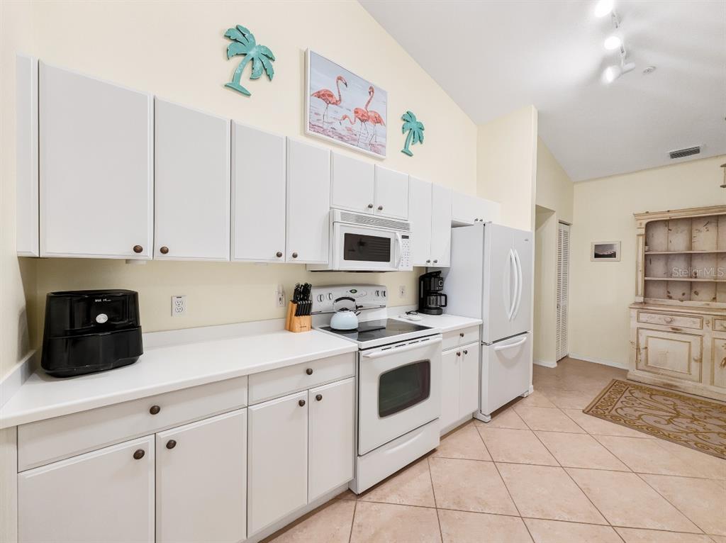 A kitchen features white cabinets, white appliances, a light countertop, and tile flooring — 8175 CELESTE DRIVE UNIT 1229, NAPLES, FL