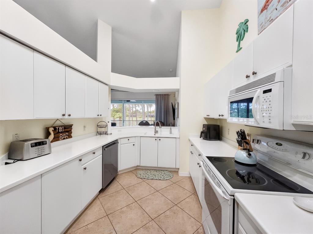 A galley-style kitchen features white cabinetry, tile flooring, and a view of the outdoors — 8175 CELESTE DRIVE UNIT 1229, NAPLES, FL