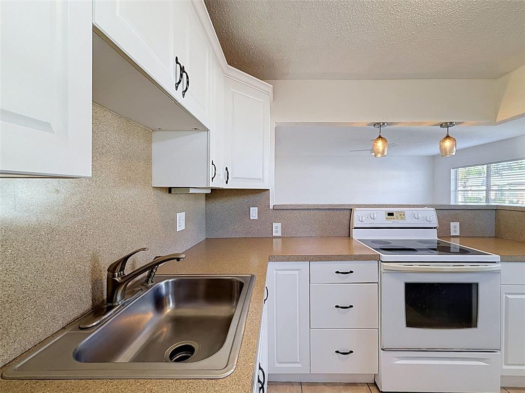 A kitchen features white cabinets, a stainless steel sink, a white stove, and speckled countertops — 11921 BOYNTON LANE UNIT 53A, NEW PORT RICHEY, FL