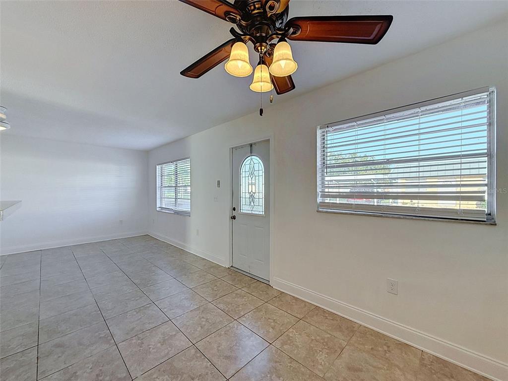 A room with white walls, tiled floors, a ceiling fan, and a front door — 11921 BOYNTON LANE UNIT 53A, NEW PORT RICHEY, FL