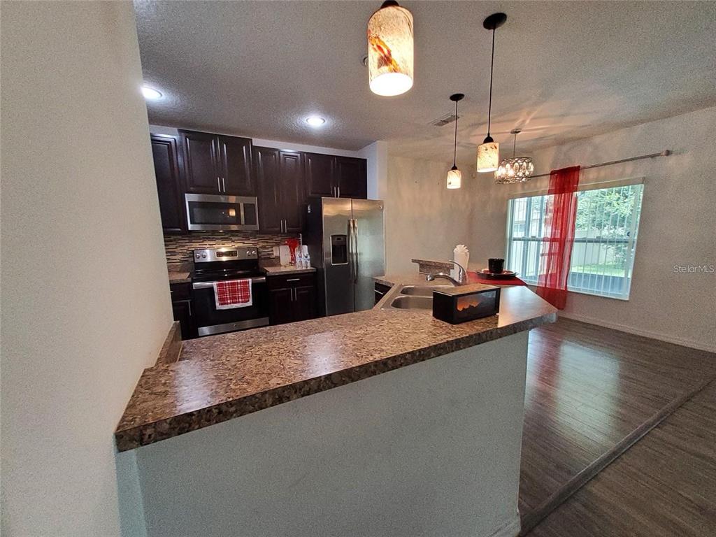 A kitchen features dark wood cabinets, stainless steel appliances, and a granite-topped breakfast bar — 355 GRANADA BOULEVARD, DAVENPORT, FL
