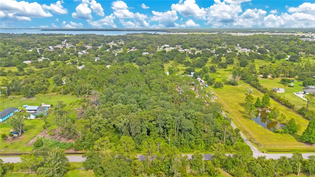 An aerial view shows a wooded lot with a pond, nearby houses, and a distant lake — 3641 PACKARD AVENUE, ST CLOUD, FL