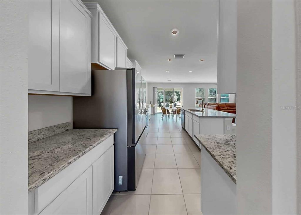 A kitchen with white cabinets, granite countertops, and stainless steel appliances leads to a dining area — 16454 WOODSIDE GLEN, PARRISH, FL