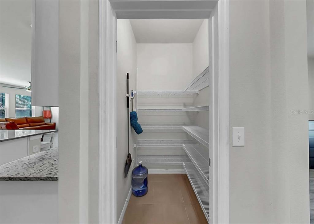 A walk-in pantry features white wire shelving, tiled flooring, and a wall-mounted cleaning tool rack — 16454 WOODSIDE GLEN, PARRISH, FL