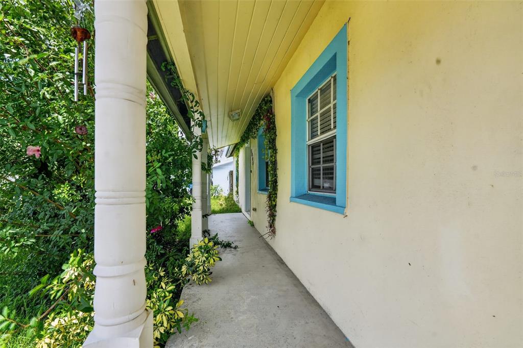 A covered concrete porch runs along the side of a yellow house with blue-trimmed windows — 5005 STOLLS AVENUE, TAMPA, FL