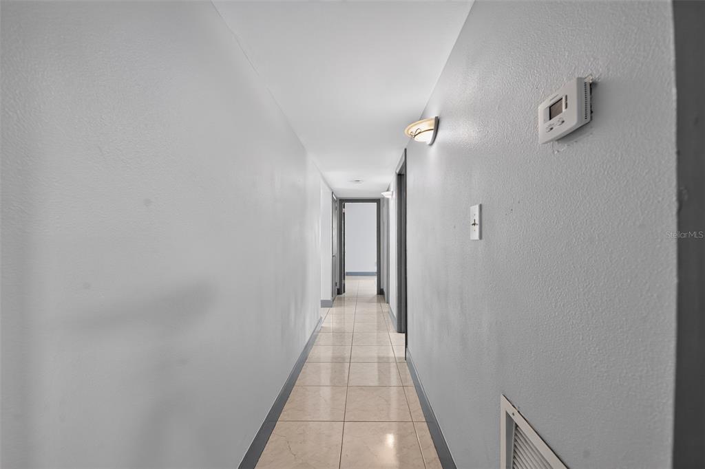A hallway with light-colored tile flooring, gray walls, and a light fixture on the ceiling — 5005 STOLLS AVENUE, TAMPA, FL