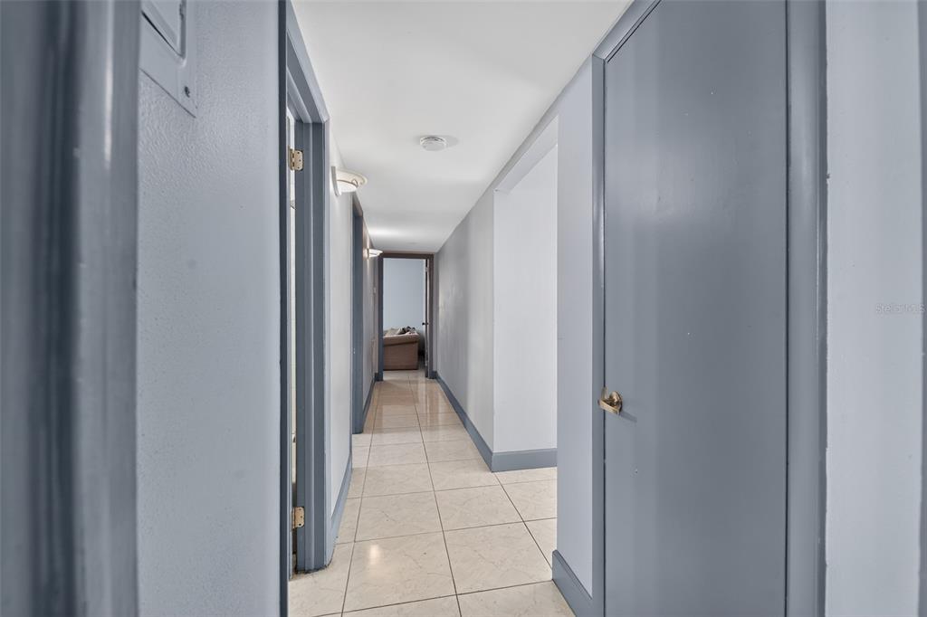 A hallway with light-colored tile flooring, gray walls, and several closed interior doors — 5005 STOLLS AVENUE, TAMPA, FL