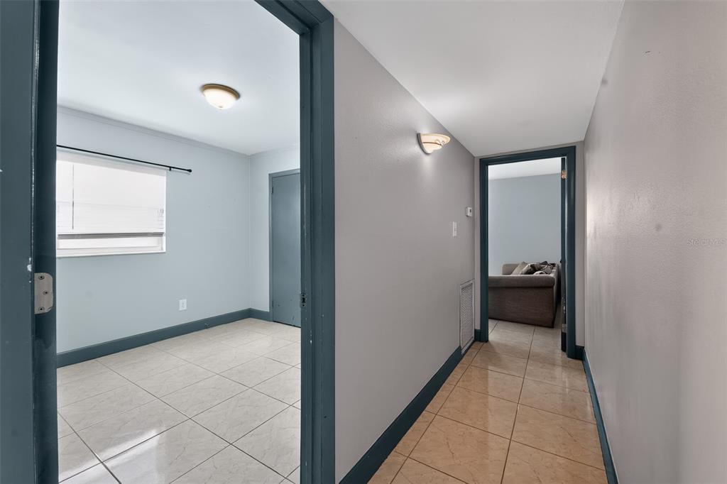 A hallway with tile flooring leads to two rooms with light blue walls and doorways — 5005 STOLLS AVENUE, TAMPA, FL