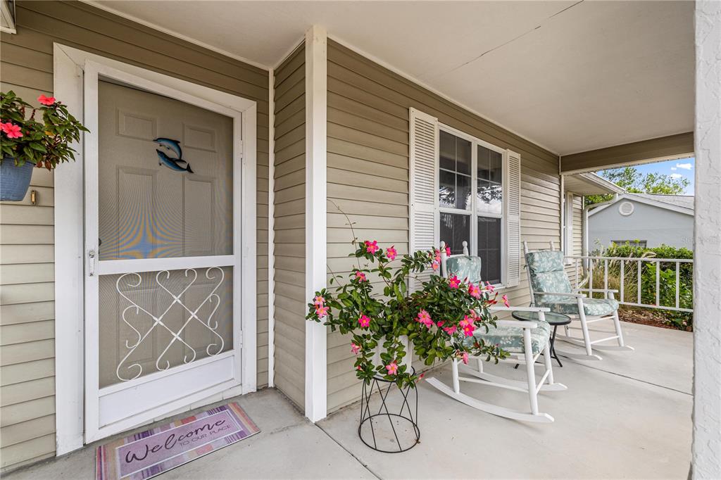 A covered front porch features light siding, two rocking chairs, and a screen door — 8137 SW 117TH LOOP, OCALA, FL