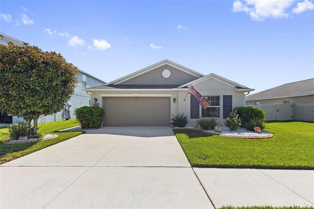 A single-story suburban house with a two-car garage, beige stucco siding, and a manicured lawn — 1749 BROAD WINGED HAWK DRIVE, RUSKIN, FL