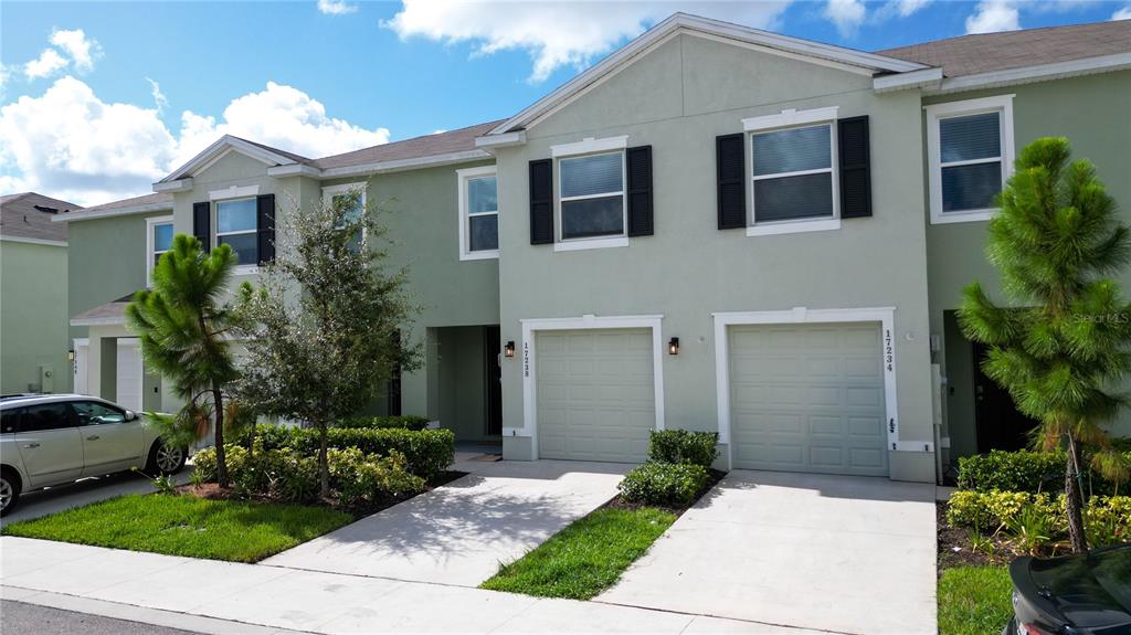 A two-story townhouse exterior features light green stucco, two garage doors, and small front lawns — 17238 AMBER ASPEN WAY, LAND O LAKES, FL