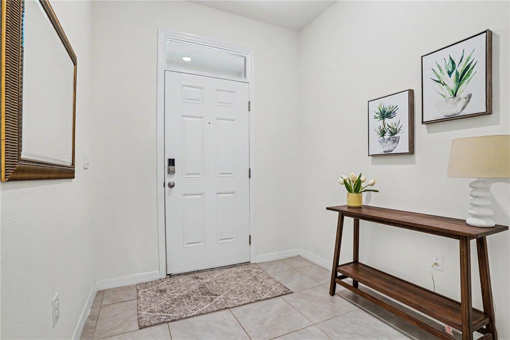 An entryway features a white front door, tiled flooring, a console table, and wall art — 17238 AMBER ASPEN WAY, LAND O LAKES, FL