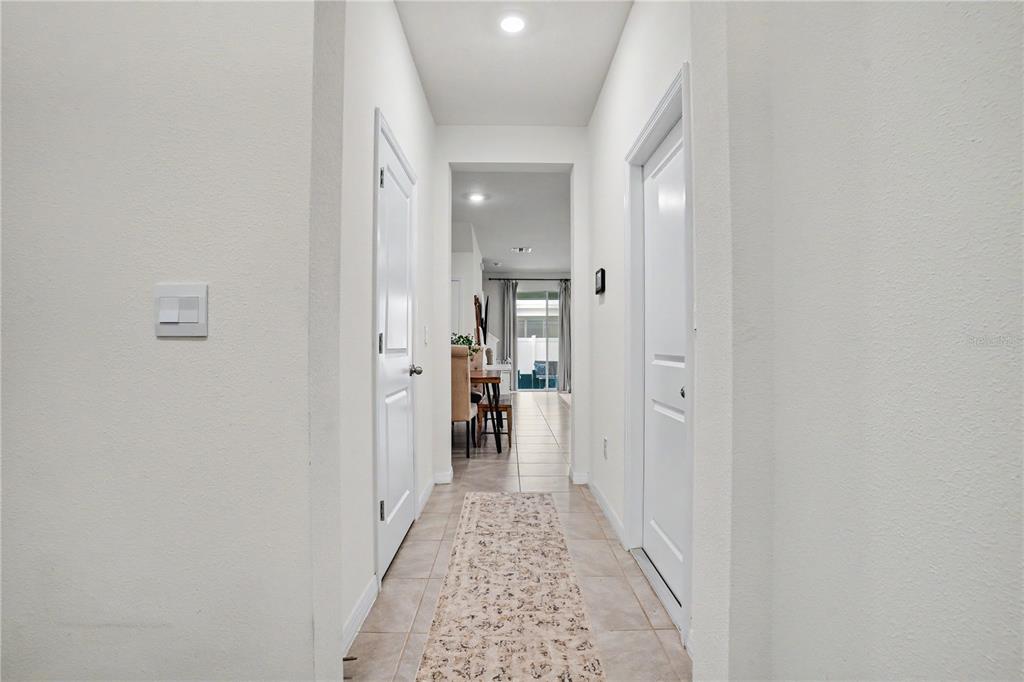 A hallway with light tile flooring leads toward a dining area and sliding glass doors — 17238 AMBER ASPEN WAY, LAND O LAKES, FL