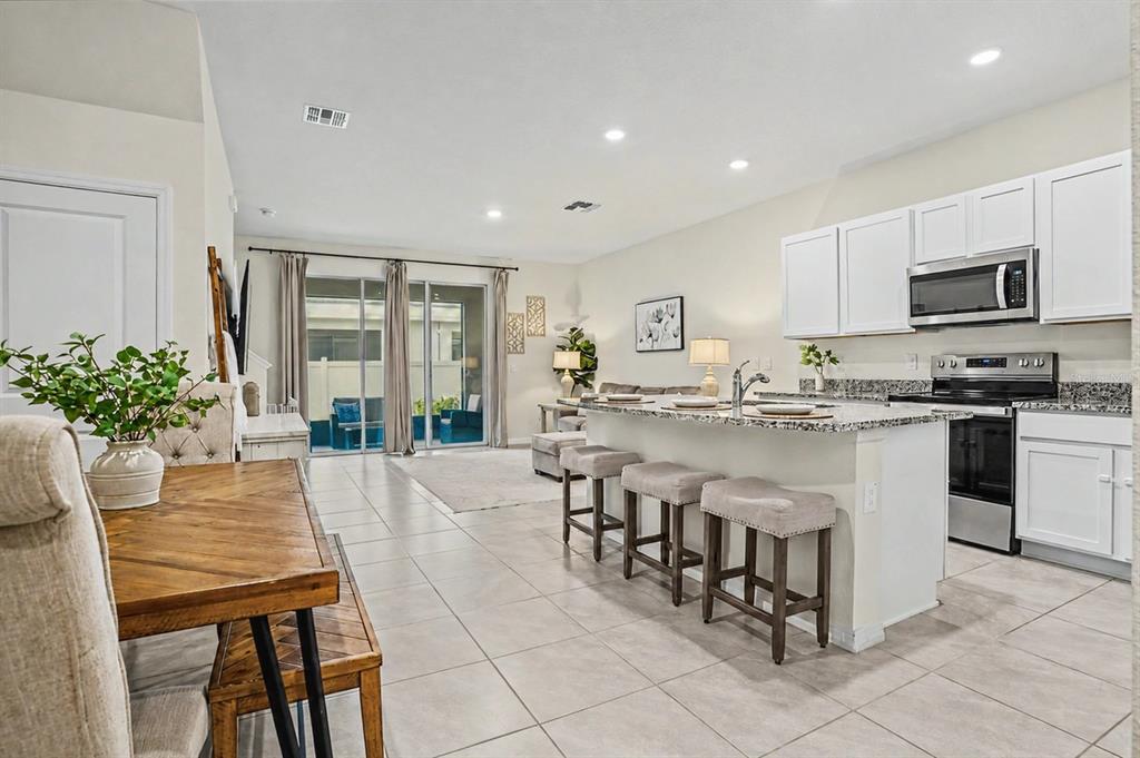 An open-concept kitchen and living area featuring white cabinets, granite countertops, and tile flooring — 17238 AMBER ASPEN WAY, LAND O LAKES, FL