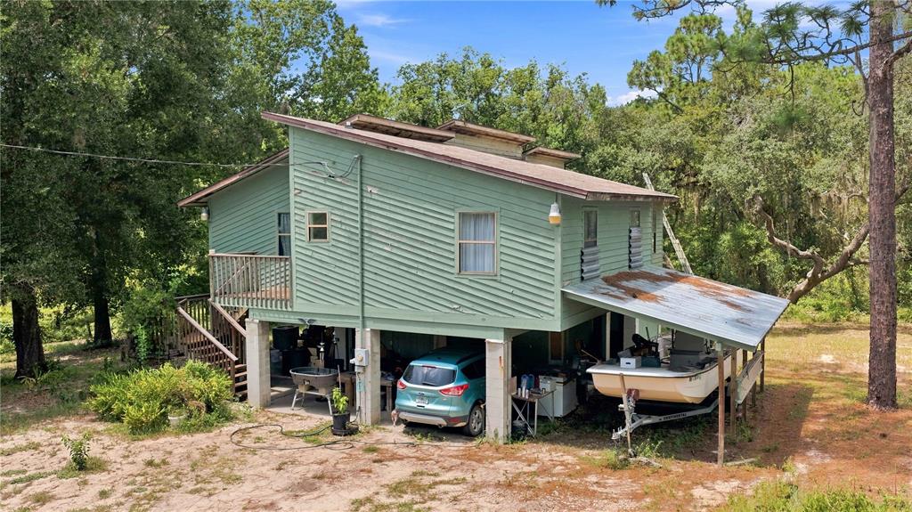 An elevated green house with a covered parking area, a boat on a trailer, and stairs — 5257 N SATIN TERRACE, DUNNELLON, FL