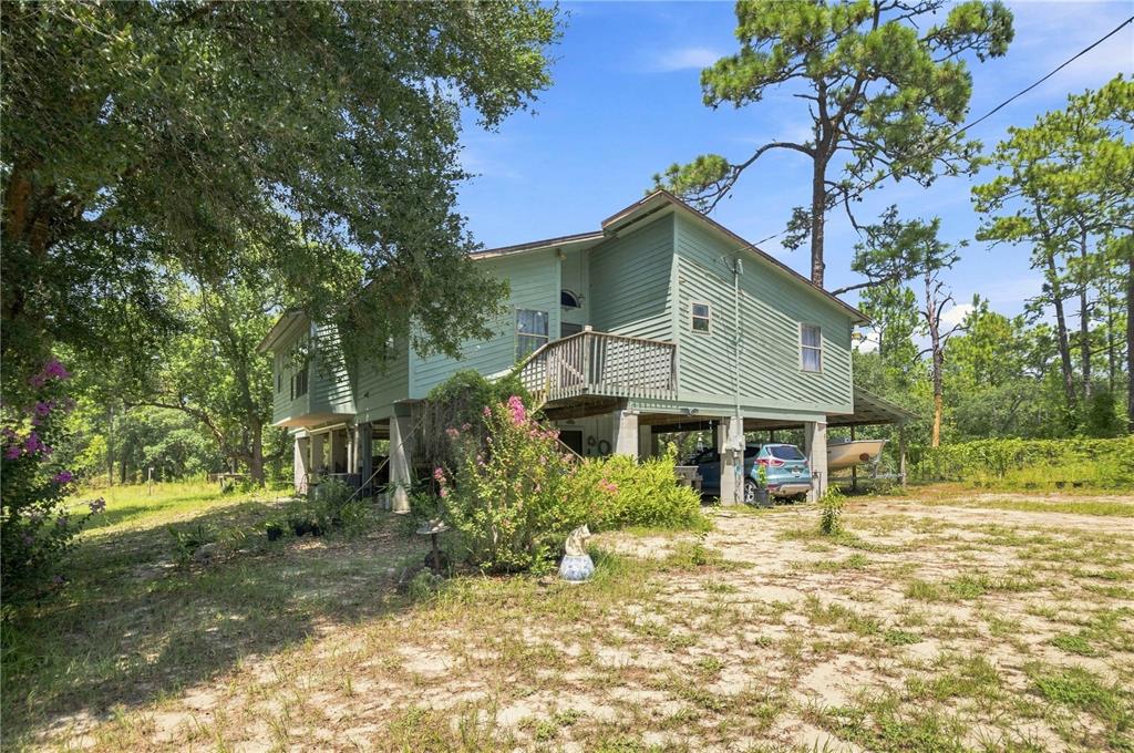 A light green elevated house stands on concrete pilings surrounded by trees and sandy ground — 5257 N SATIN TERRACE, DUNNELLON, FL