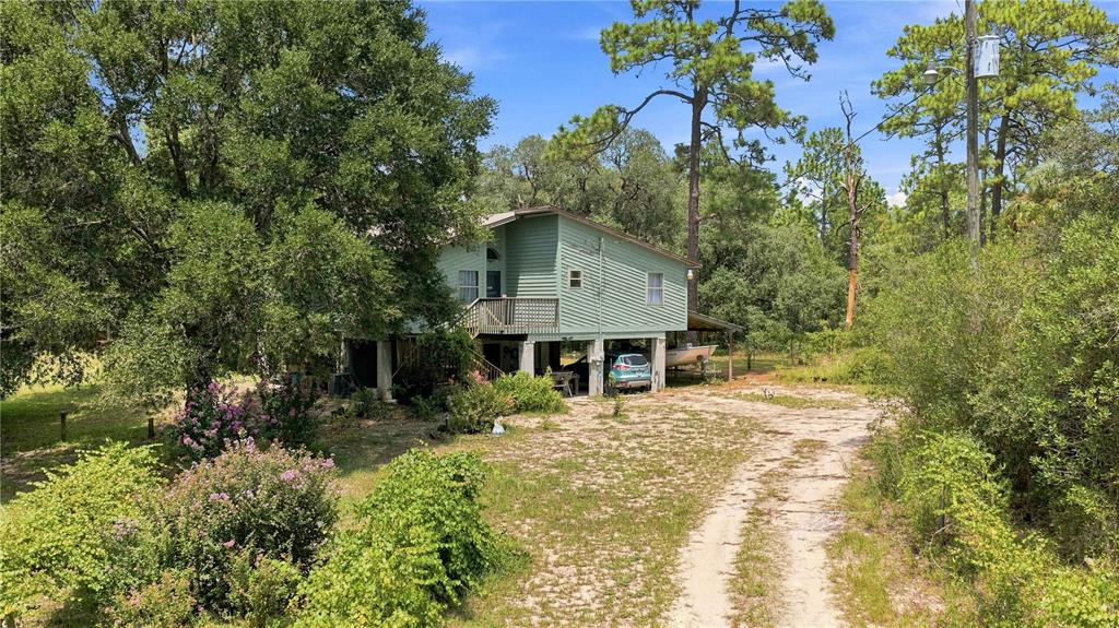 A light green house on stilts sits in a wooded lot with a dirt driveway — 5257 N SATIN TERRACE, DUNNELLON, FL