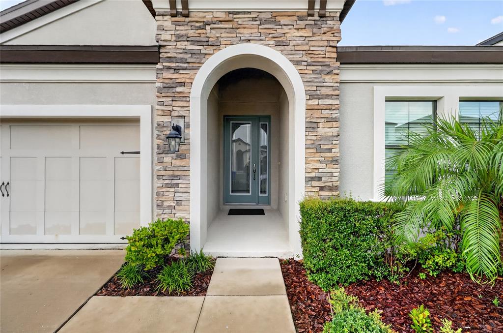 The exterior of a house features a stone-accented arched entryway, a garage, and landscaping — 12635 SHETLAND WALK DRIVE, LITHIA, FL