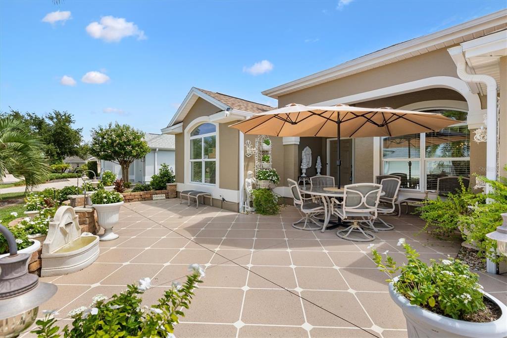 A patio with a dining set under an umbrella, a fountain, and potted plants — 2493 BACHMAN PATH, THE VILLAGES, FL