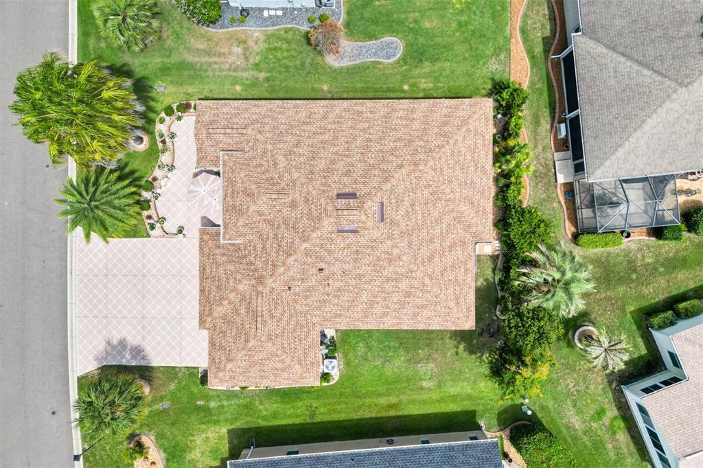 An aerial view shows a residential house with a brown shingled roof and paved patio — 2493 BACHMAN PATH, THE VILLAGES, FL