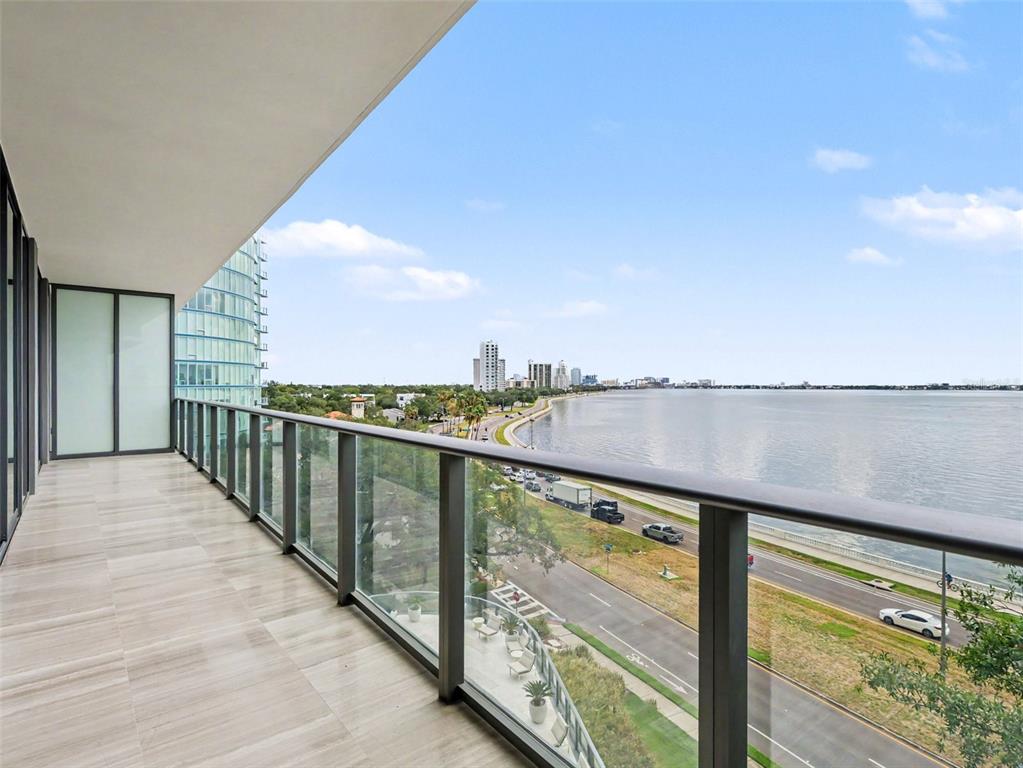 A modern balcony with glass railings overlooks a coastal road and a large body of water — 3101 W BAYSHORE STREET UNIT 503, TAMPA, FL