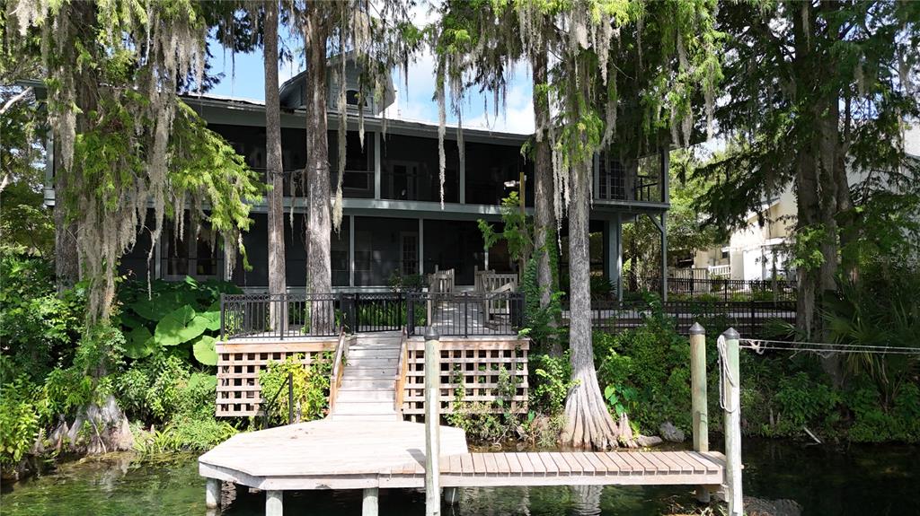 A two-story house with a screened porch sits behind a wooden dock on the water — 11685 E BLUE COVE DRIVE, DUNNELLON, FL